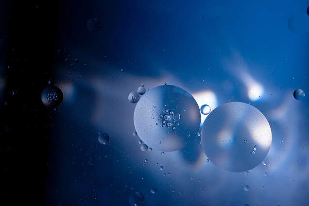 Abstract image of translucent oil droplets suspended in blue liquid, illuminated by light reflections and shadows, creating a soft, ethereal effect.